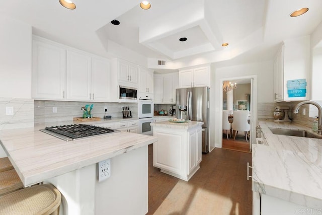 kitchen with light stone counters, a peninsula, a sink, appliances with stainless steel finishes, and white cabinetry