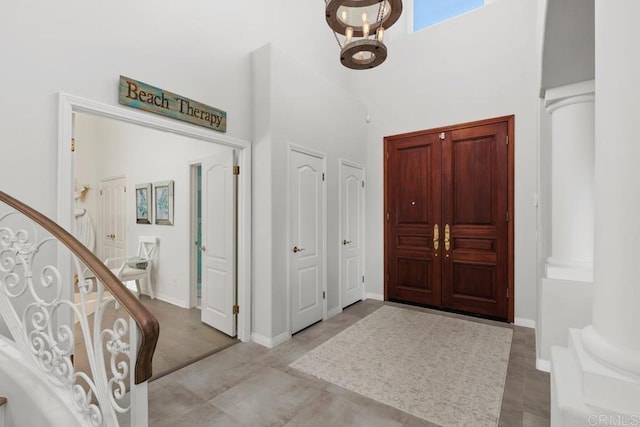 entryway with decorative columns, baseboards, a towering ceiling, and stairs