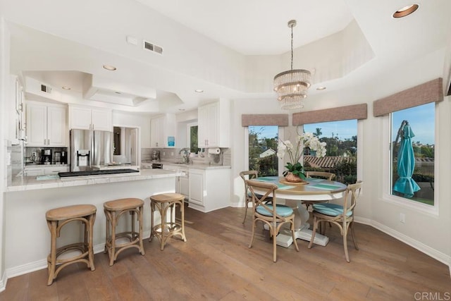 dining space with visible vents, a notable chandelier, wood finished floors, baseboards, and a raised ceiling