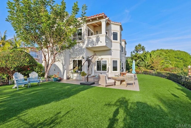 rear view of house with a balcony, fence, a tiled roof, a patio area, and a lawn