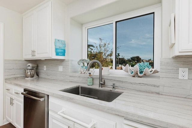 kitchen with light stone countertops, dishwasher, decorative backsplash, white cabinetry, and a sink