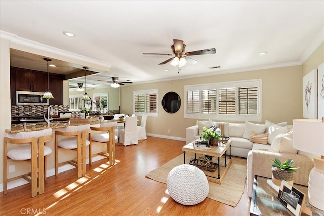 living room featuring baseboards, visible vents, light wood-style flooring, recessed lighting, and ornamental molding