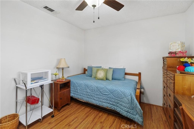 bedroom with ceiling fan, wood finished floors, visible vents, and a textured ceiling