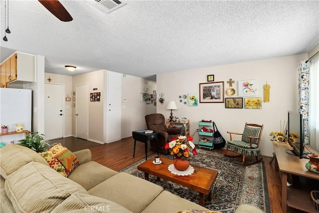 living area featuring a textured ceiling, wood finished floors, visible vents, and ceiling fan