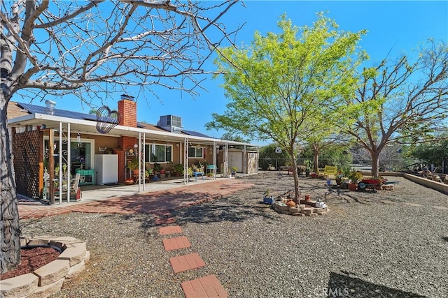 back of house featuring central AC, a patio area, roof mounted solar panels, and a chimney