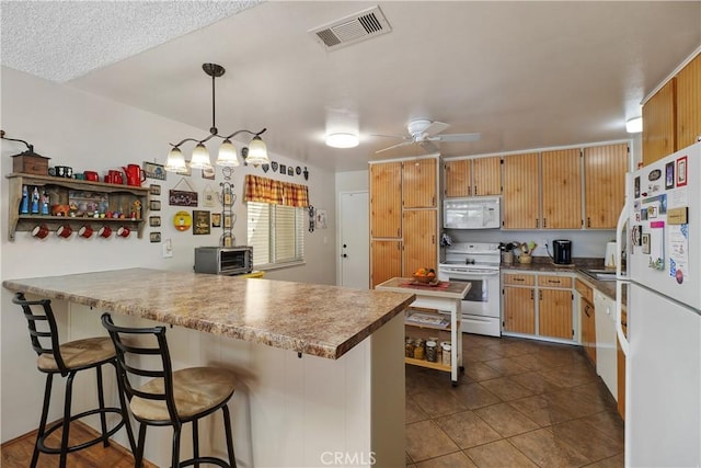 kitchen with white appliances, visible vents, a peninsula, a kitchen breakfast bar, and dark tile patterned floors