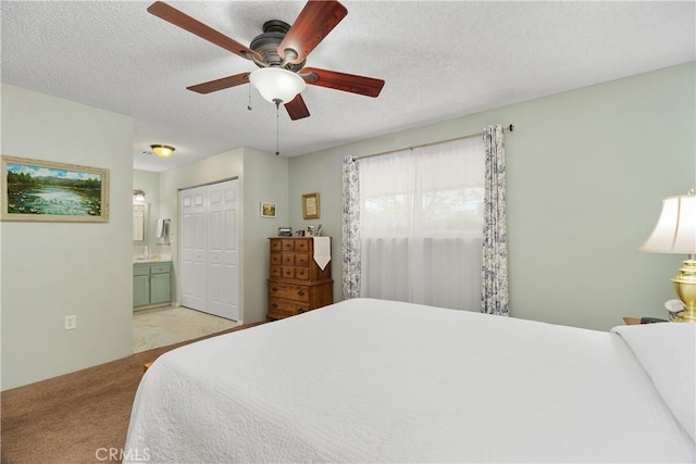 bedroom featuring ceiling fan, light colored carpet, ensuite bathroom, a closet, and a textured ceiling