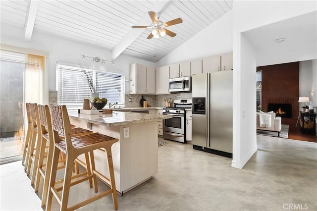 kitchen featuring beamed ceiling, a breakfast bar, stainless steel appliances, a brick fireplace, and backsplash