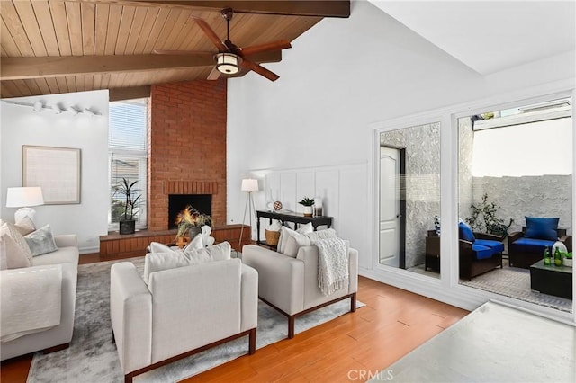 living room featuring beam ceiling, ceiling fan, light wood-style floors, wooden ceiling, and a brick fireplace