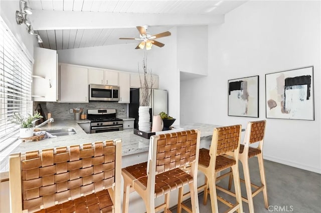 kitchen with tasteful backsplash, vaulted ceiling with beams, appliances with stainless steel finishes, white cabinetry, and a sink