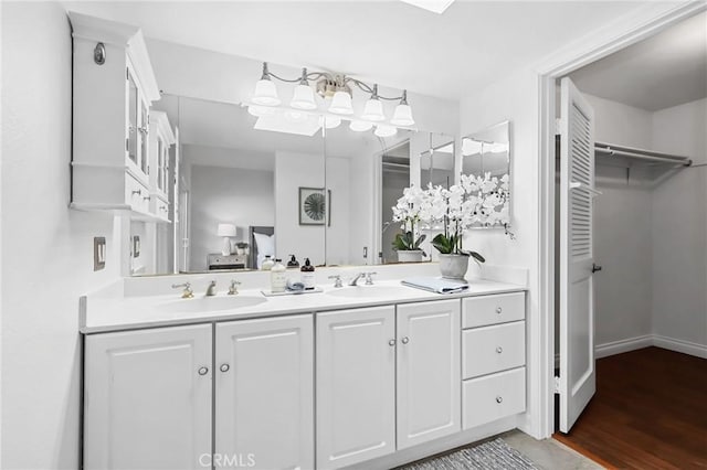 bathroom featuring double vanity, a spacious closet, wood finished floors, and a sink