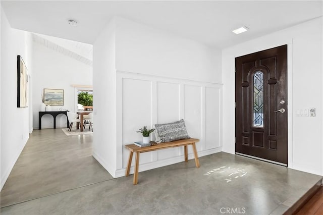 entryway with lofted ceiling, a decorative wall, and finished concrete floors