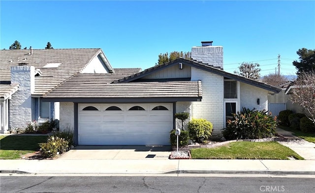 view of front of property with driveway, a tile roof, a garage, brick siding, and a chimney