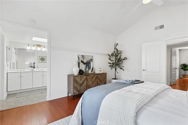 bedroom featuring visible vents, connected bathroom, light wood-type flooring, vaulted ceiling, and a sink