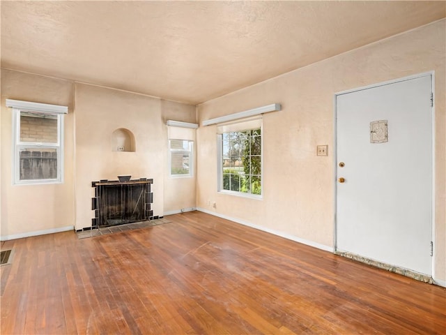 unfurnished living room with hardwood / wood-style flooring, a fireplace, baseboards, and visible vents