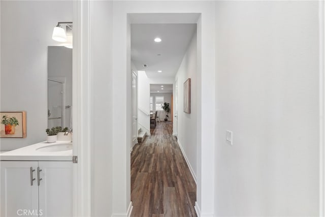 corridor with dark wood-style floors, recessed lighting, baseboards, and a sink