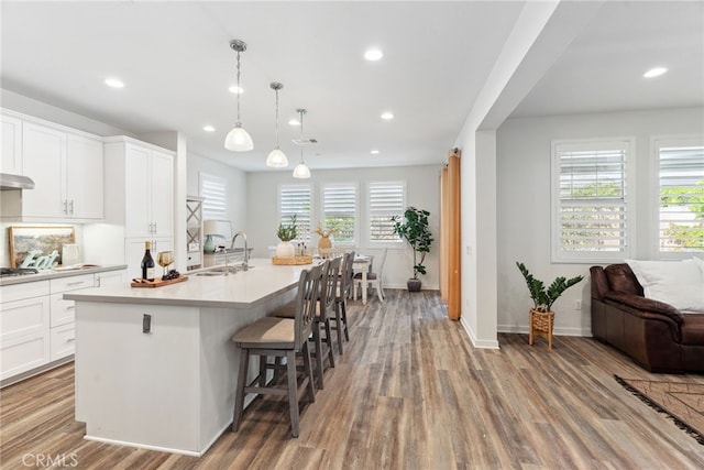 kitchen featuring a sink, wood finished floors, an island with sink, and light countertops