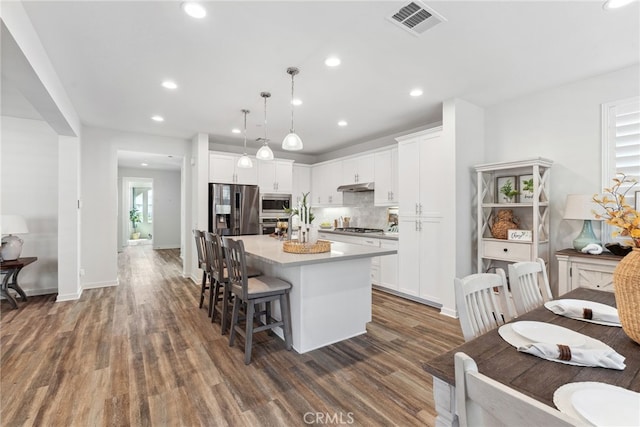 kitchen with a center island, dark wood-type flooring, under cabinet range hood, decorative backsplash, and appliances with stainless steel finishes