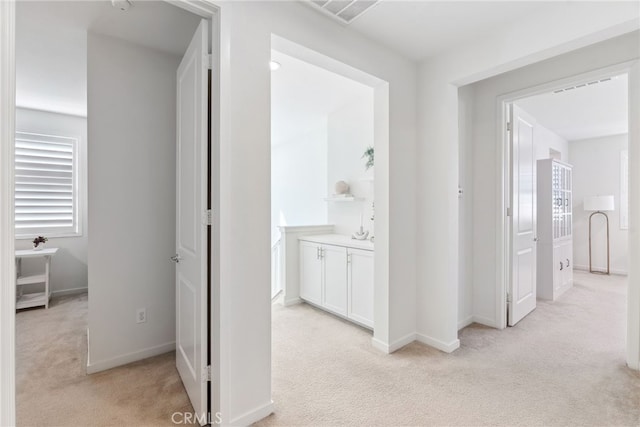 hall with baseboards, visible vents, and light carpet