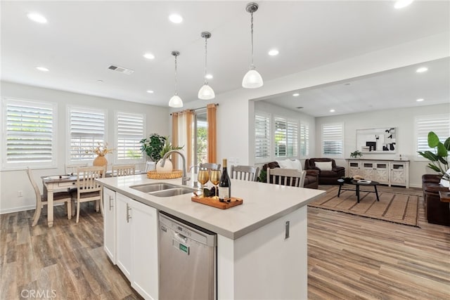 kitchen with visible vents, an island with sink, a sink, stainless steel dishwasher, and wood finished floors