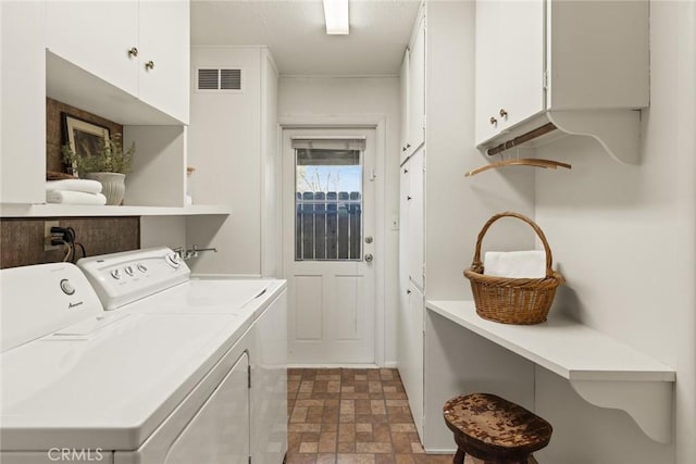 laundry room with washer and dryer, visible vents, cabinet space, and stone finish floor