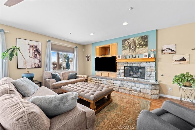 living room with a stone fireplace, recessed lighting, baseboards, and wood finished floors