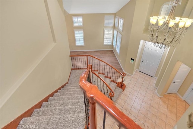 stairway featuring baseboards, a high ceiling, a chandelier, and tile patterned flooring