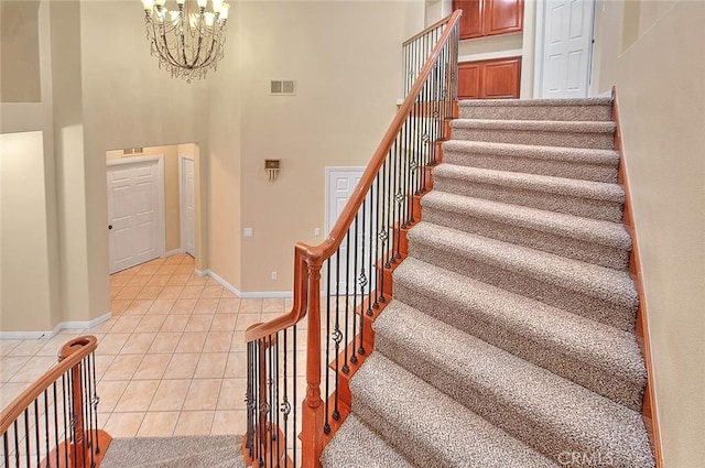 staircase featuring visible vents, a high ceiling, an inviting chandelier, tile patterned flooring, and baseboards