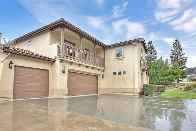 mediterranean / spanish-style house featuring a tile roof, stucco siding, driveway, a balcony, and an attached garage