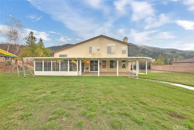 back of property with a playground, stucco siding, a chimney, a yard, and a patio