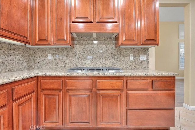 kitchen with stainless steel gas stovetop, light stone counters, tasteful backsplash, and under cabinet range hood