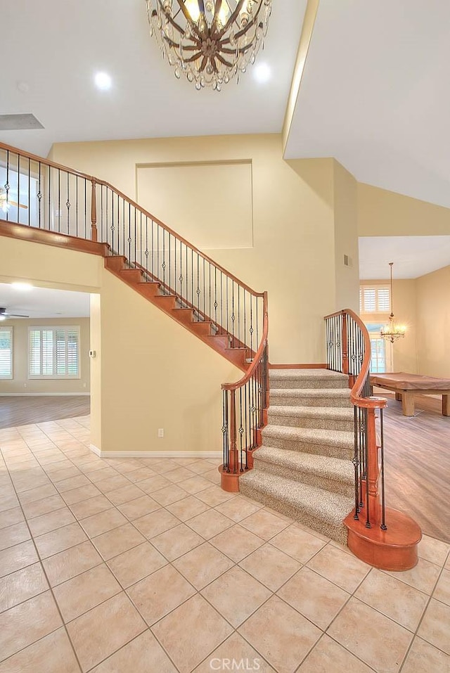 stairway with baseboards, a notable chandelier, a towering ceiling, and tile patterned flooring