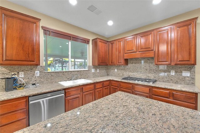 kitchen with tasteful backsplash, appliances with stainless steel finishes, light stone counters, and a sink