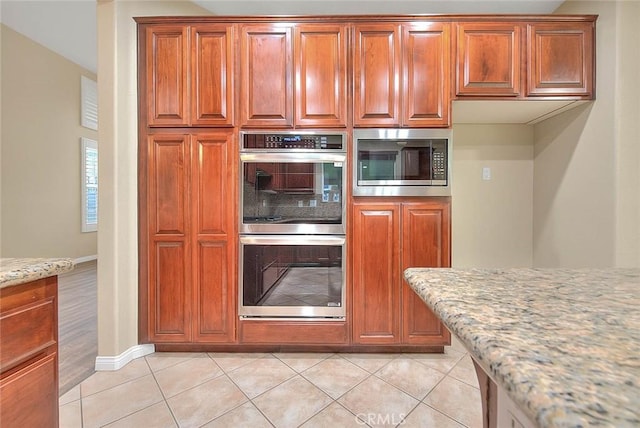 kitchen with light stone counters, stainless steel appliances, light tile patterned flooring, and brown cabinetry