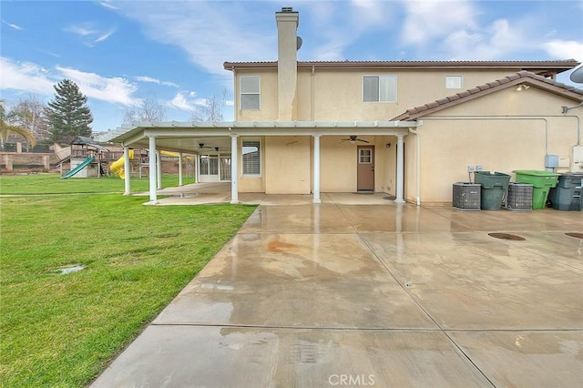 rear view of house with a playground, ceiling fan, stucco siding, a lawn, and a patio