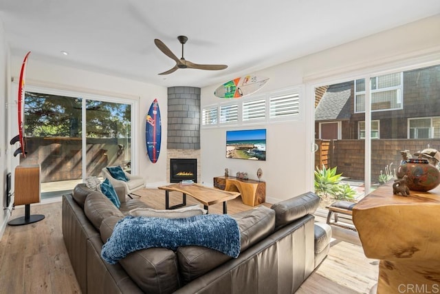 living room featuring baseboards, a large fireplace, a ceiling fan, and wood finished floors