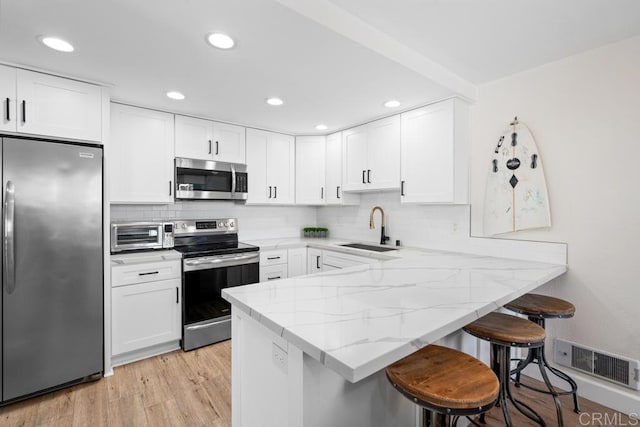 kitchen with visible vents, a breakfast bar area, light stone counters, appliances with stainless steel finishes, and a sink