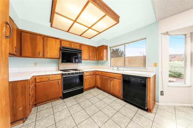 kitchen featuring brown cabinetry, light tile patterned flooring, black appliances, and a sink