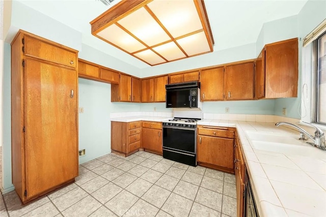 kitchen featuring a sink, tile counters, black microwave, range with gas cooktop, and brown cabinets