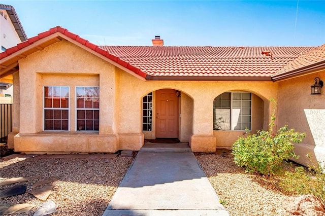 doorway to property with stucco siding, a porch, a chimney, and a tile roof