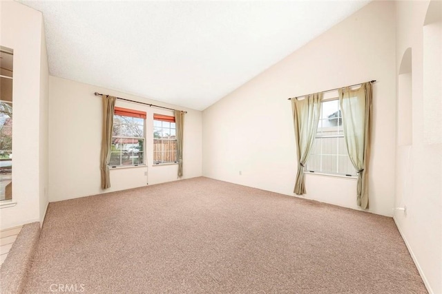 carpeted spare room featuring vaulted ceiling and arched walkways