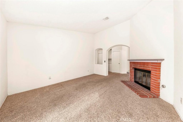 unfurnished living room with arched walkways, visible vents, a fireplace, and carpet floors