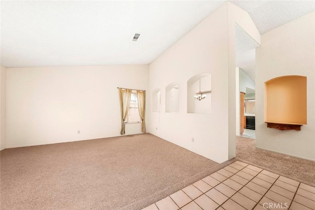 unfurnished room with visible vents, light tile patterned floors, light colored carpet, a chandelier, and vaulted ceiling