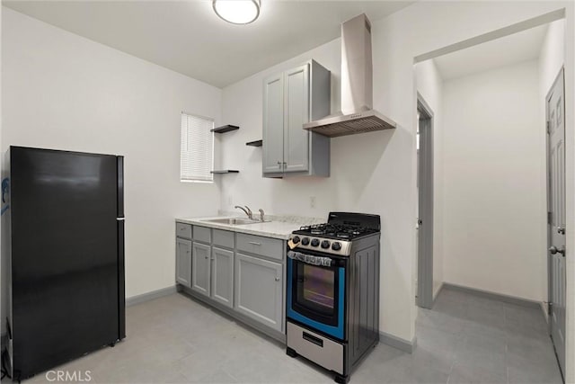 kitchen with stainless steel gas range, freestanding refrigerator, a sink, gray cabinetry, and wall chimney exhaust hood