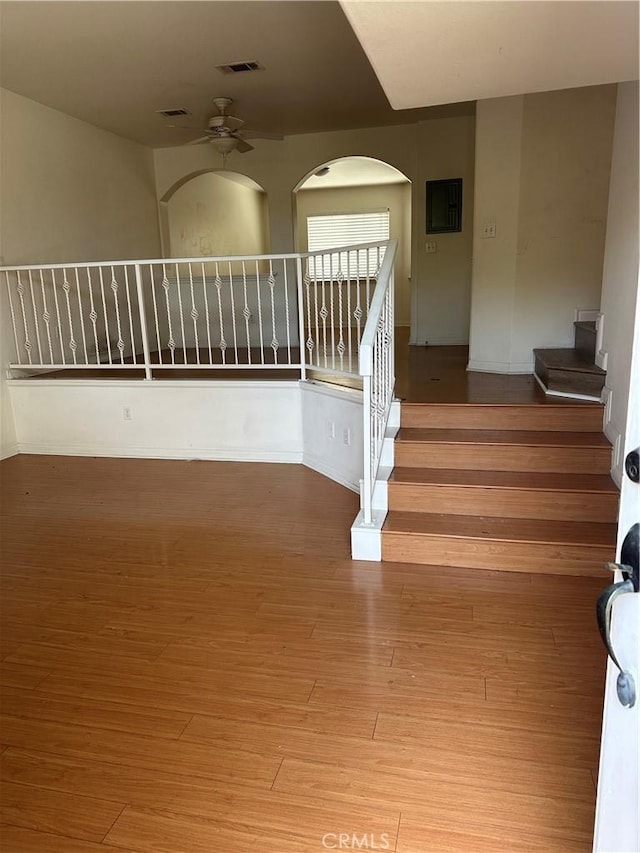 staircase featuring visible vents, electric panel, wood finished floors, arched walkways, and ceiling fan