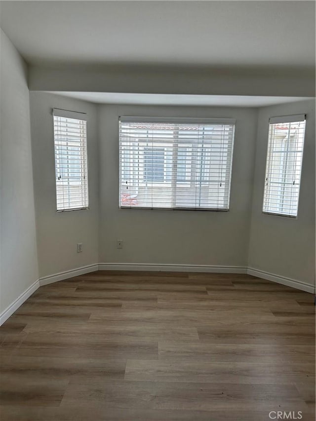 empty room with plenty of natural light, baseboards, and wood finished floors