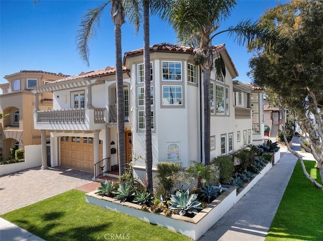 mediterranean / spanish house with a tile roof, stucco siding, decorative driveway, a balcony, and an attached garage