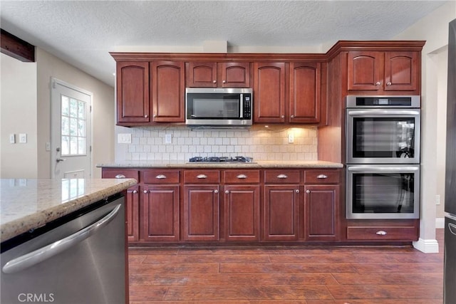 kitchen with light stone counters, stainless steel appliances, tasteful backsplash, and dark wood-style floors