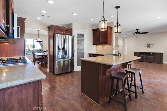 kitchen featuring visible vents, a sink, dark wood-style floors, stainless steel appliances, and a peninsula