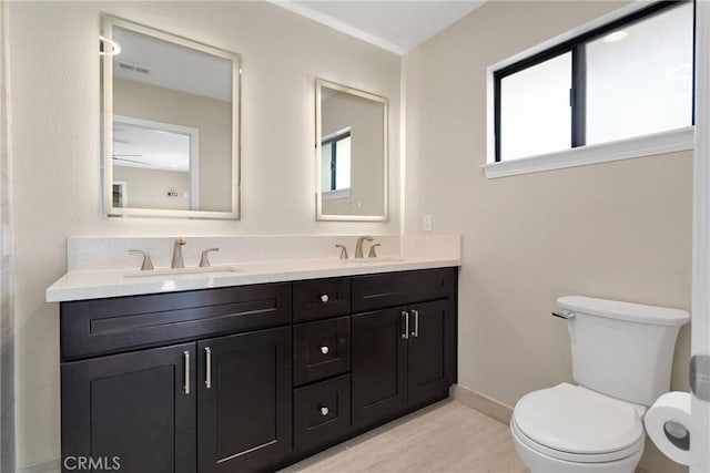 bathroom with double vanity, visible vents, toilet, and a sink